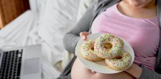A pregnant woman holding a plate full of donuts.
