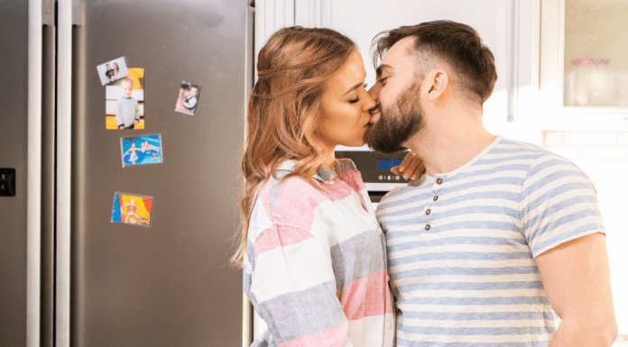 A man and woman kissing in the kitchen.