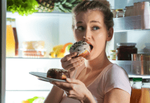 A woman eating donuts in front of the refridgerator.