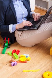 Woman sitting on floor and typing on laptop surrounded by kids toys