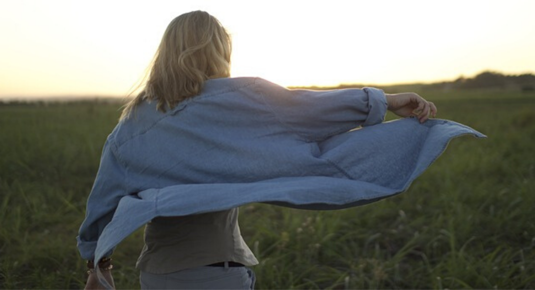A woman standing in a field with her shirt blowing.
