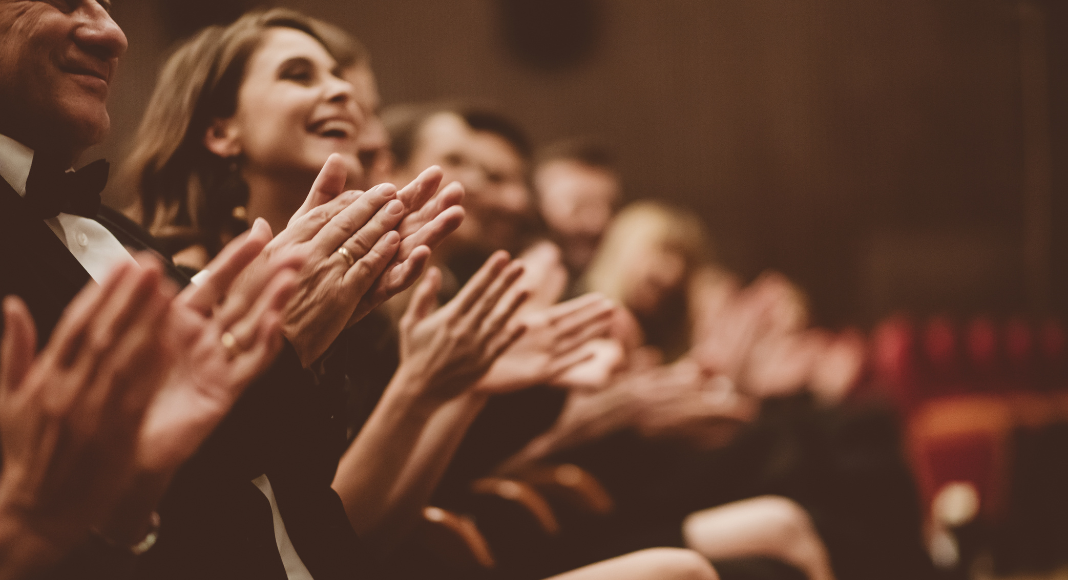 Audience members clapping in a theater.