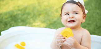 A toddler sitting in a tub holding a rubber ducky.