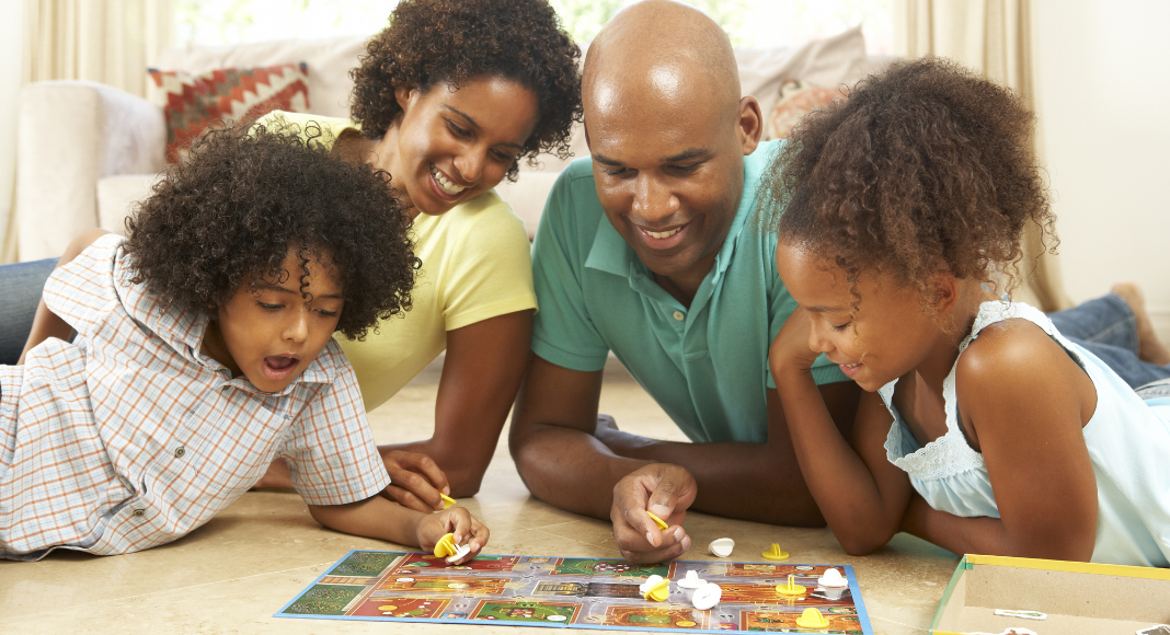 A family playing a board game laying on the floor. 