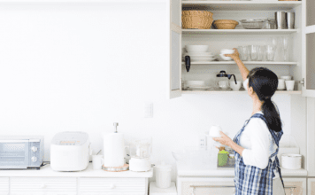 A woman putting items in a kitchen shelf.