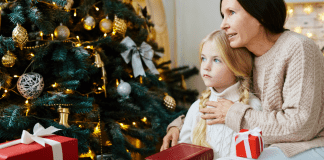 A mom holding a little girl in front of the Christmas tree.