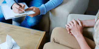 A woman sitting with her hands crossed with a therapist.