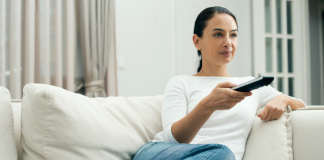 A woman holding a TV remote while sitting on the couch.