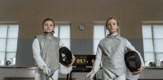 Two girls dressed in fencing gear.