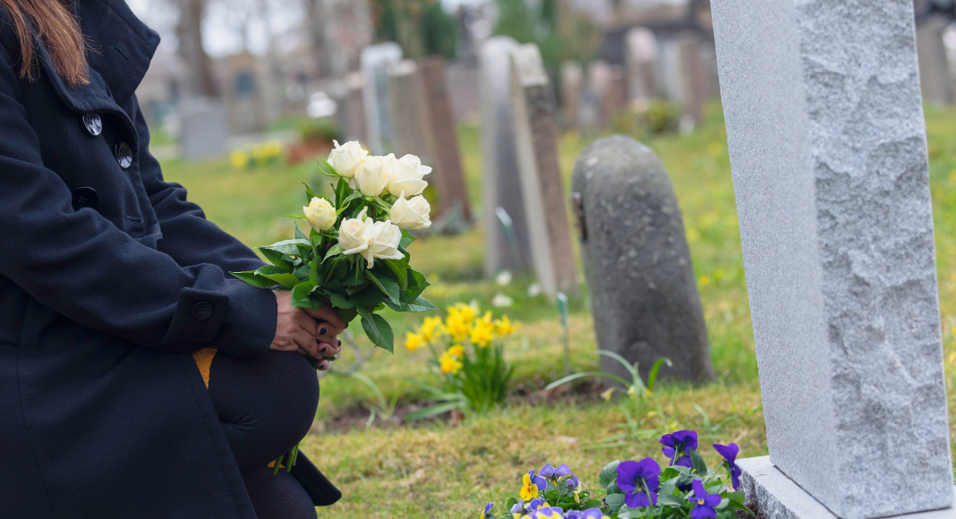 A woman putting flowers on a gravestone. 