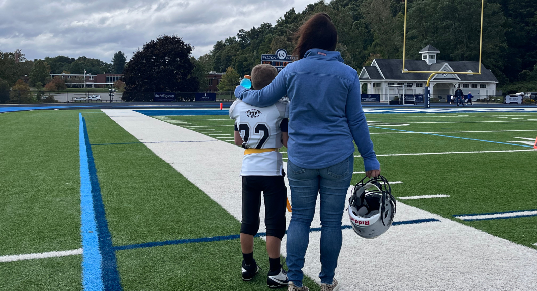A mom with her arm around her son on a football field.