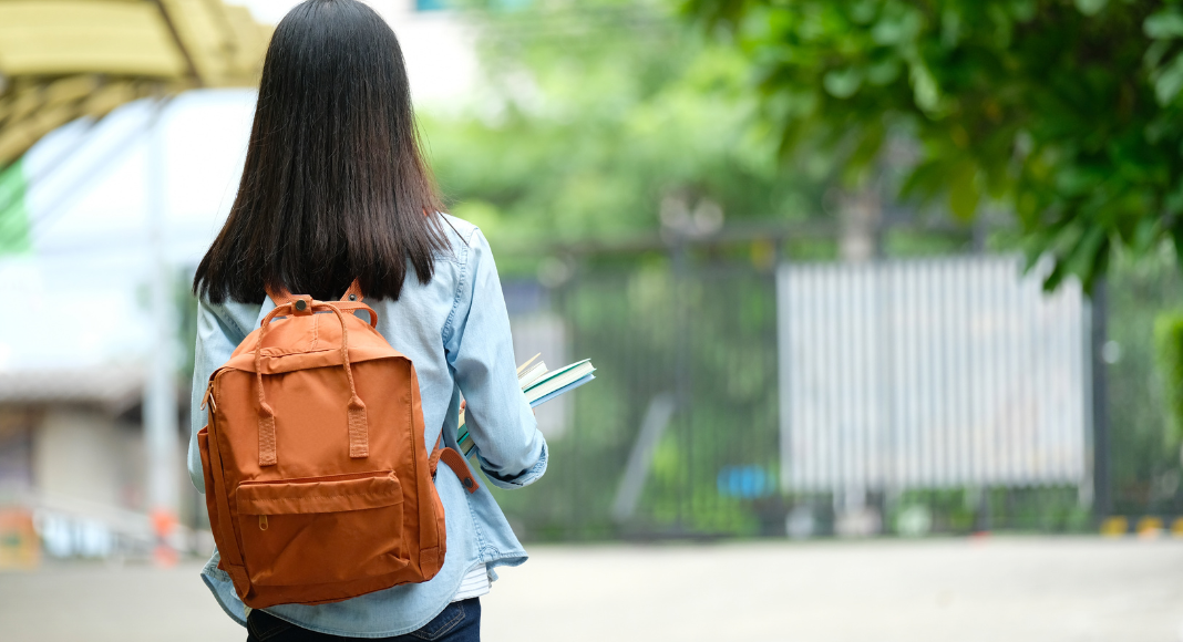 A girl standing with a backpack and holding books.