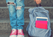 A girl standing next to her backpack.