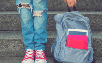 A girl standing next to her backpack.