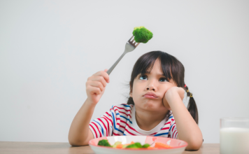 A girl looking at a piece of broccoli on her fork.