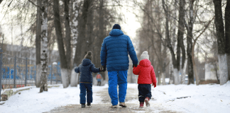 A dad walking outside holding two boys hands in the winter.