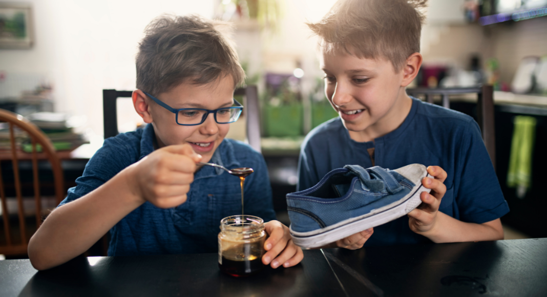Two boys pouring syrup into a shoe.