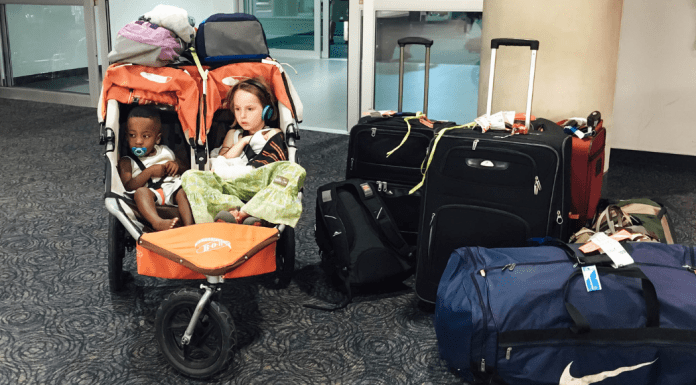 Two girls in a double stroller next to a pile of luggage.